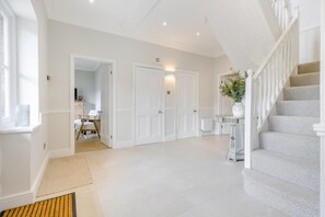Un hall d’entrée spacieux avec un escalier, des portes blanches et une petite table sur laquelle est posé un vase.