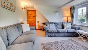 A cozy living room with a grey sofa, a wooden door, a small table, and a window with curtains. - 4 Bed in South Walsham (oc-2081) (South Walsham)