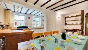 A kitchen with a brick island, wooden chairs, and a table set for breakfast with bowls, mugs, and a coffee maker. - 4 Bed in South Walsham (oc-2081) (South Walsham)