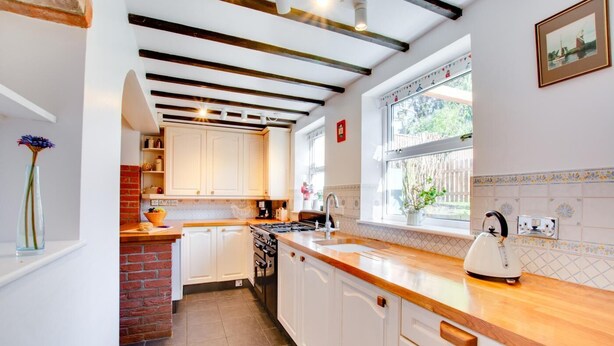 A kitchen with white cabinets, a brick wall, a wooden countertop, and a window with a view. - 4 Bed in South Walsham (oc-2081) (South Walsham)