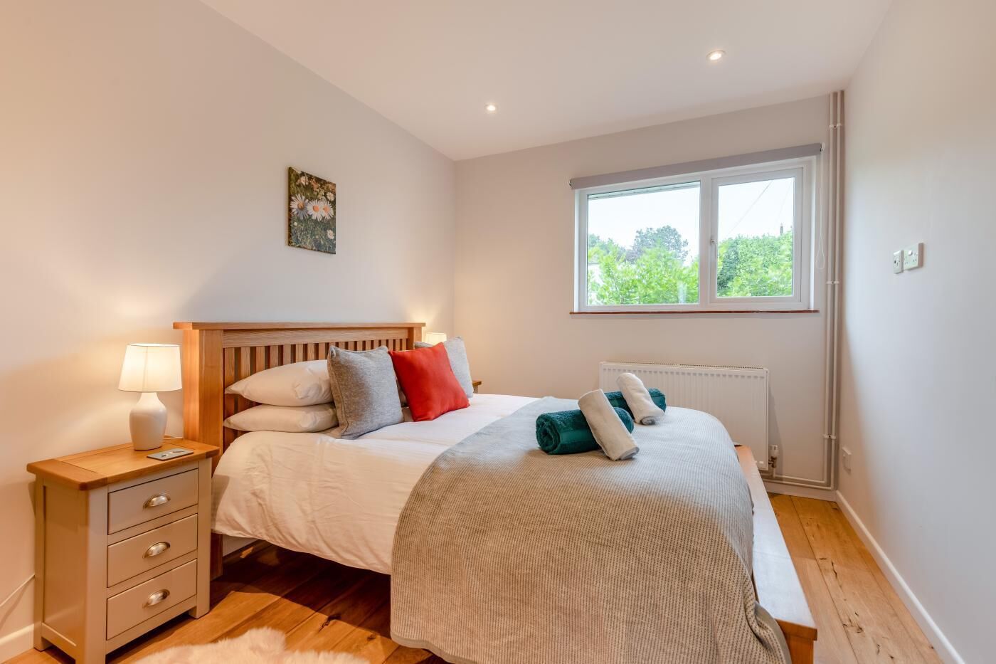 A bedroom with a bed, bedside table, lamp, and a window with a view of greenery.