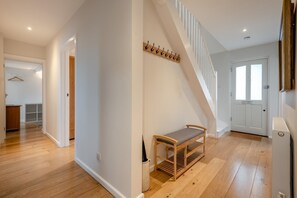 A spacious hallway with wooden flooring, a bench, a coat rack, and a staircase leading to another room. - 3 Bed in Worth Matravers (oc-h32107) (Worth Matravers)