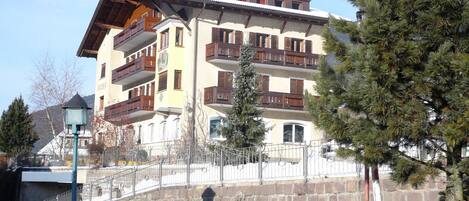 A multi-story building with balconies, a stone wall, and a snow-covered ground.