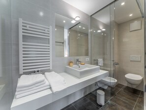 Un baño moderno con cabina de ducha de vidrio, tocador blanco con lavamanos y espejo, y un inodoro.