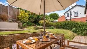 An outdoor wooden table set for breakfast with plates, croissants, and orange juice, under a large umbrella. - 4 Bed in Ruswarp (oc-d32269) (Ruswarp)