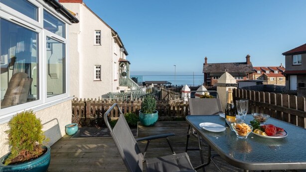 A terrace with a table set for dining, overlooking a coastal area. - 3 Bed in Sandsend (oc-wa241) (Sandsend)