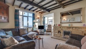 A cozy living room with a stone fireplace, leather sofas, a television, and a large window overlooking the sea. - 3 Bed in Sandsend (oc-wa241) (Sandsend)