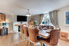 Een eethoek met een houten tafel, lederen stoelen en een aan de muur bevestigde televisie.
