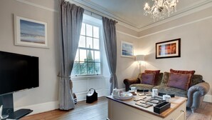 A cozy living room with a flat-screen TV, a wooden coffee table, a sofa with cushions, and a chandelier. - 4 Bed in Whitby (oc-w474) (Whitby)