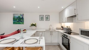 Une cuisine moderne avec des meubles blancs, un coin repas agrémenté d’une chaise rouge et un tableau accroché au mur.