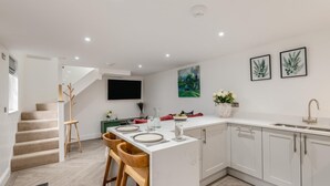 Une cuisine moderne avec des meubles blancs, un îlot central doté de tabourets de bar, une table à manger et un escalier menant à un autre niveau.
