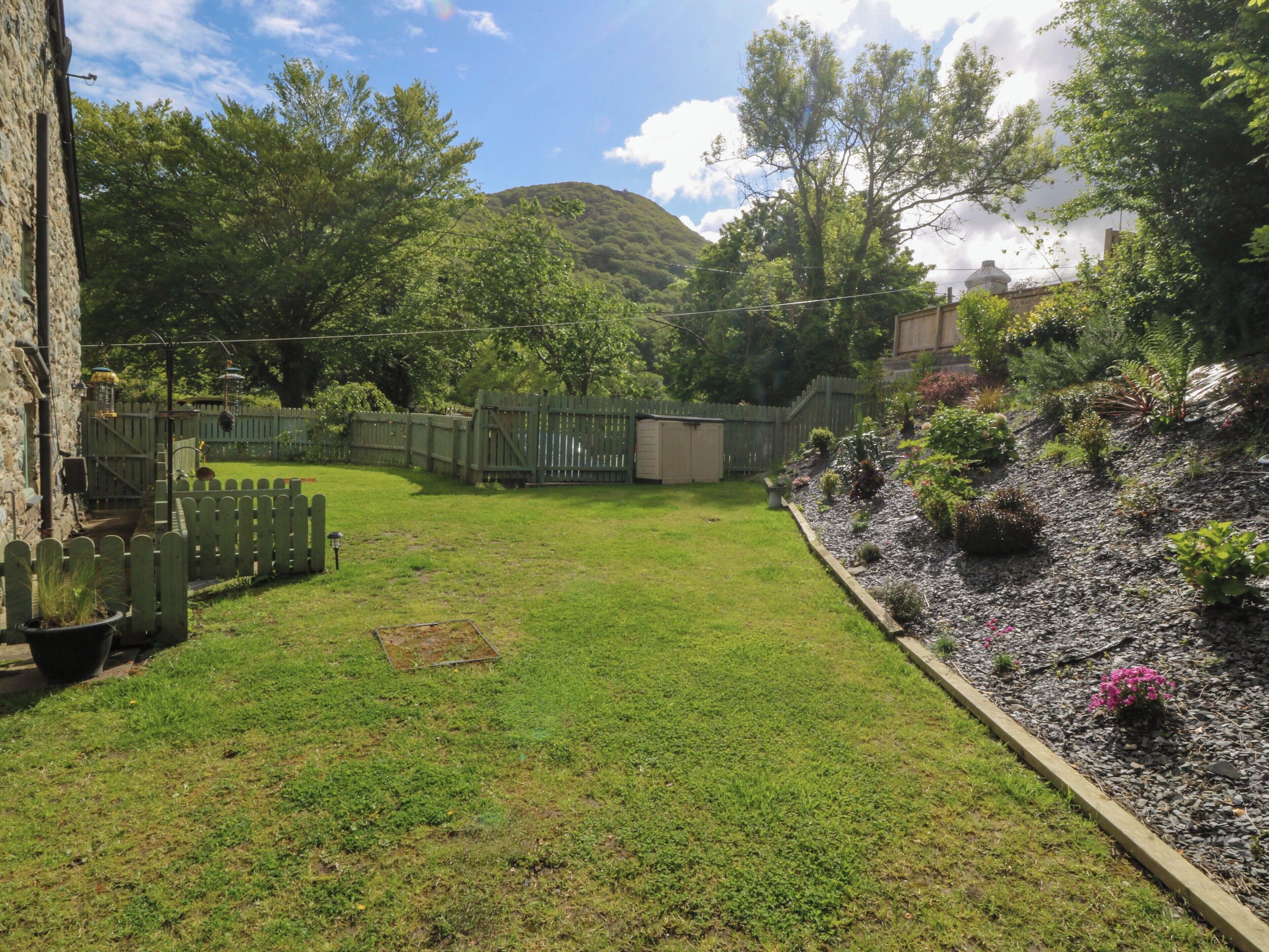 Ein Garten mit Rasen, Holzzaun und Blumenbeeten mit verschiedenen Pflanzen.