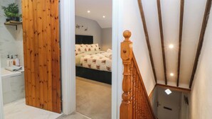 A bedroom with a bed, a wooden door, a bathroom with a sink, and a staircase with wooden balusters. - Old Chapel House (Llanfairfechan)