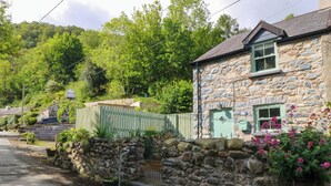 A stone house with a green door, a stone wall, and a garden with pink flowers. - Old Chapel House (Llanfairfechan)