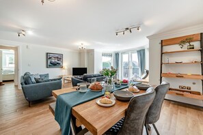 A modern living room with a dining area, a sofa, a TV, and a bookshelf. - 2 Bed in Tenby (oc-b32277) (Tenby)