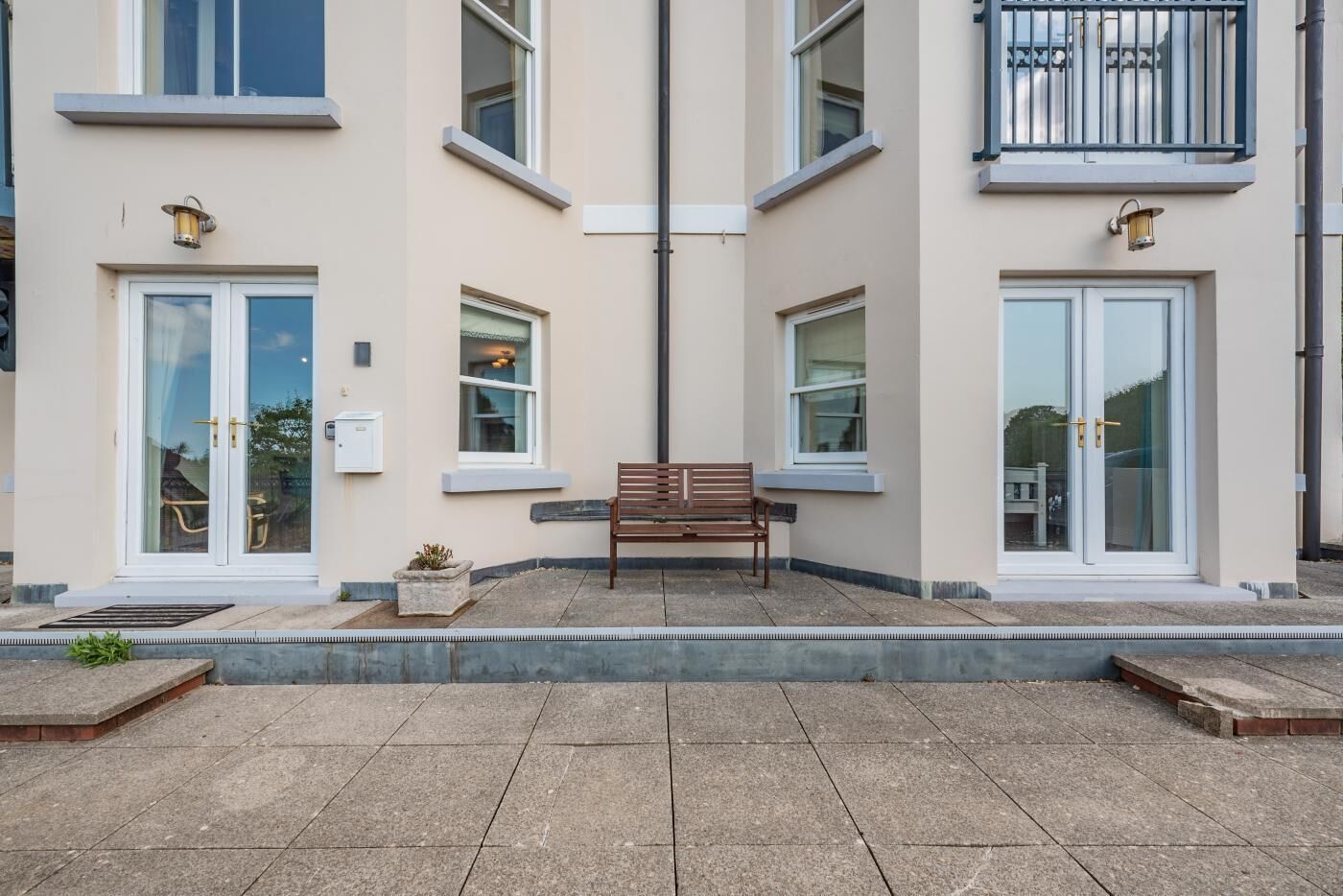 A building with a bench in front of a glass door entrance, a small planter, and a window with a view.