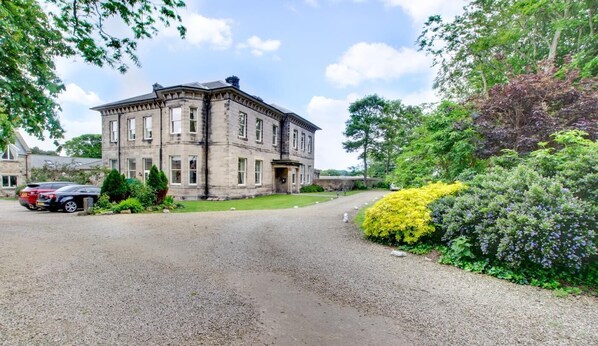 A large, historic stone building with a symmetrical facade, a gravel driveway, and lush greenery surrounding the property. - 2 Bed in Beadnell (oc-gd1869) (Beadnell)