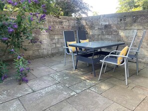 Eine Terrasse im Freien mit Tisch und Stühlen, einer Steinmauer und lila Blumen.