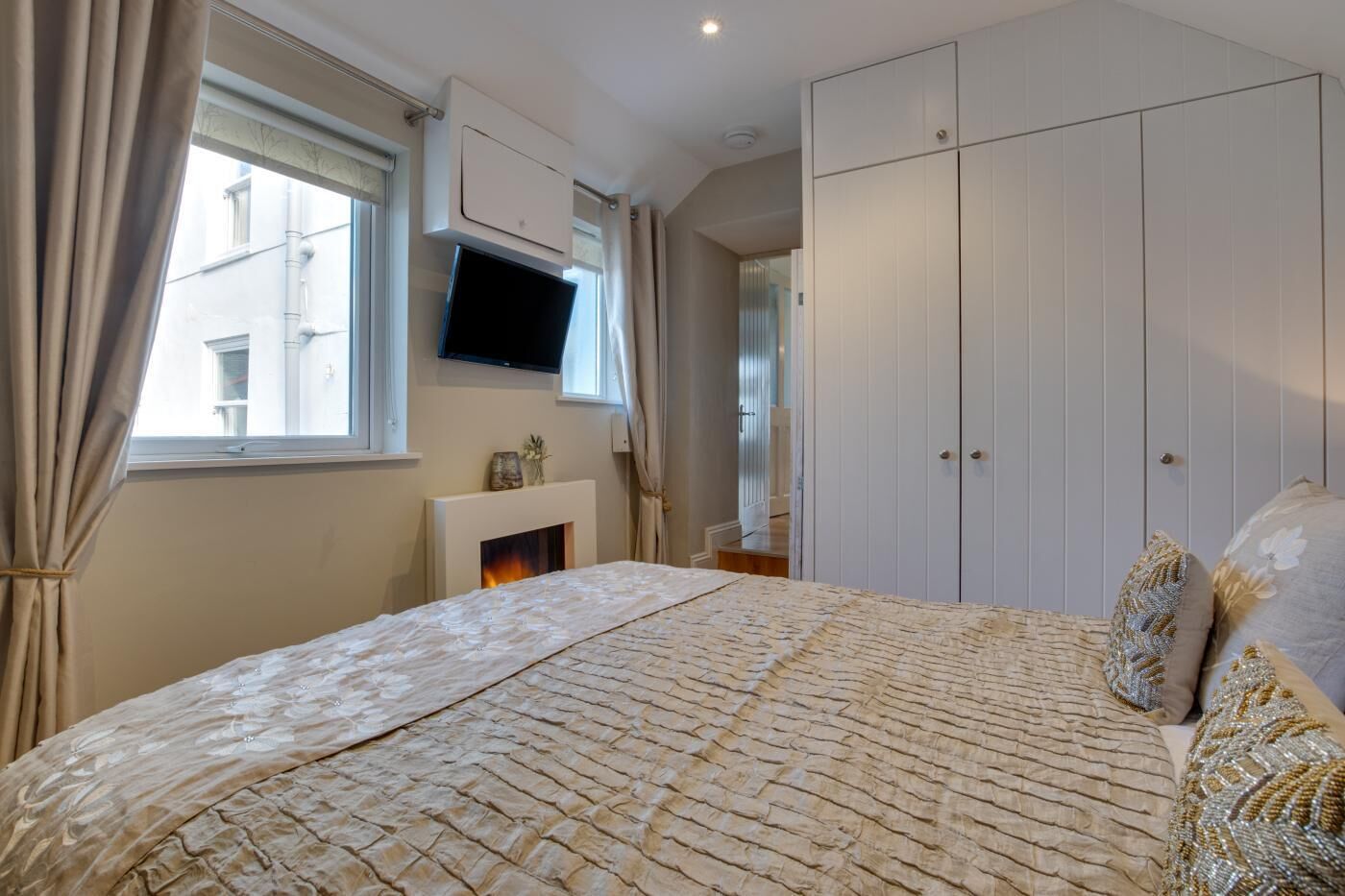Une chambre à coucher avec un lit, un téléviseur fixé au-dessus d’une cheminée et une armoire.