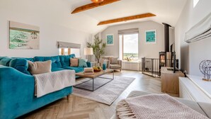 A spacious living room with a teal sofa, a wooden coffee table, and a large window offering a view of the outdoors. - 3 Bed in Mawgan Porth (oc-p00824) (Mawgan Porth)
