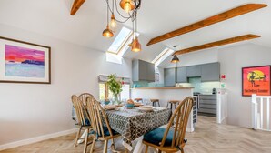 A dining area with a table set for four, wooden chairs, pendant lighting, and a view of the kitchen in the background. - 3 Bed in Mawgan Porth (oc-p00824) (Mawgan Porth)