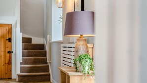 A staircase with a wooden finish, a wall-mounted lamp with a cylindrical shade, and a small potted plant. - 3 Bed in Mawgan Porth (oc-p00824) (Mawgan Porth)