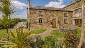 A stone building with a wooden door, windows, and a paved courtyard with plants. - 3 Bed in Mawgan Porth (oc-p00824) (Mawgan Porth)