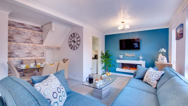 Een moderne woonkamer met een blauwe accentmuur, een open haard en een eetgedeelte met een houten wand.