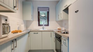 Een smalle keuken met lichtblauwe kastjes, een witte koelkast en een raam boven de gootsteen.