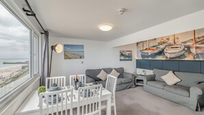 Una sala moderna con comedor, un sofá gris y un cuadro de barcos.