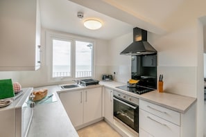 A modern kitchen with a stove, oven, and a large window overlooking the sea. - 2 Bed in Bridlington (oc-o32292) (Bridlington)