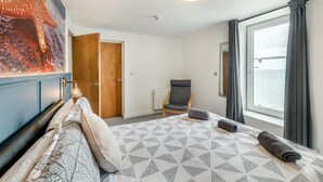 A hotel room with a bed, a chair, a large window, and a door. - 3 Bed in Bridlington (oc-o32293) (Bridlington)