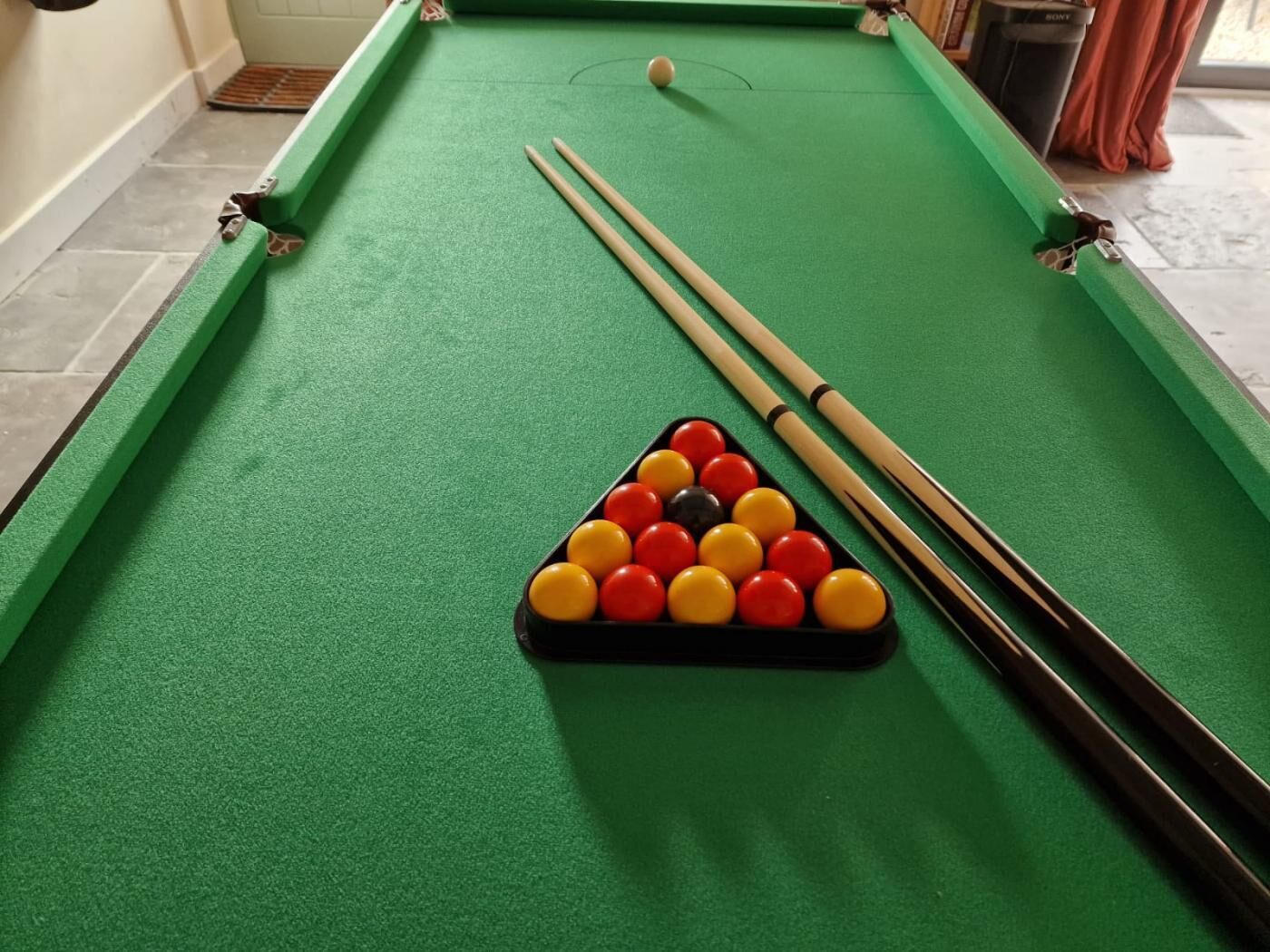 Une table de billard avec un triangle de billes, deux queues de billard et une seule bille posée sur la table.