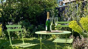 Ein Garten mit einem grünen Metalltisch und Stühlen, einer Champagnerflasche und zwei Gläsern.