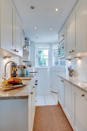A modern kitchen with white cabinetry, a granite countertop, and a view of the outdoors through a window. - 2 Bed in Southwold (oc-apco) (Southwold)