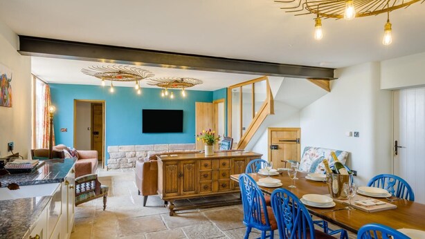 Amplia sala de estar con chimenea de piedra, una mesa de comedor de madera dispuesta para seis personas y una pared azul de acento.