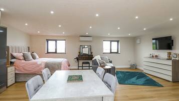 A modern, well-lit room with a bed, a dining table, a TV, and a desk.