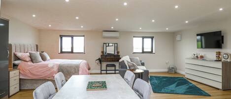 A modern, well-lit room with a bed, a dining table, a TV, and a desk.