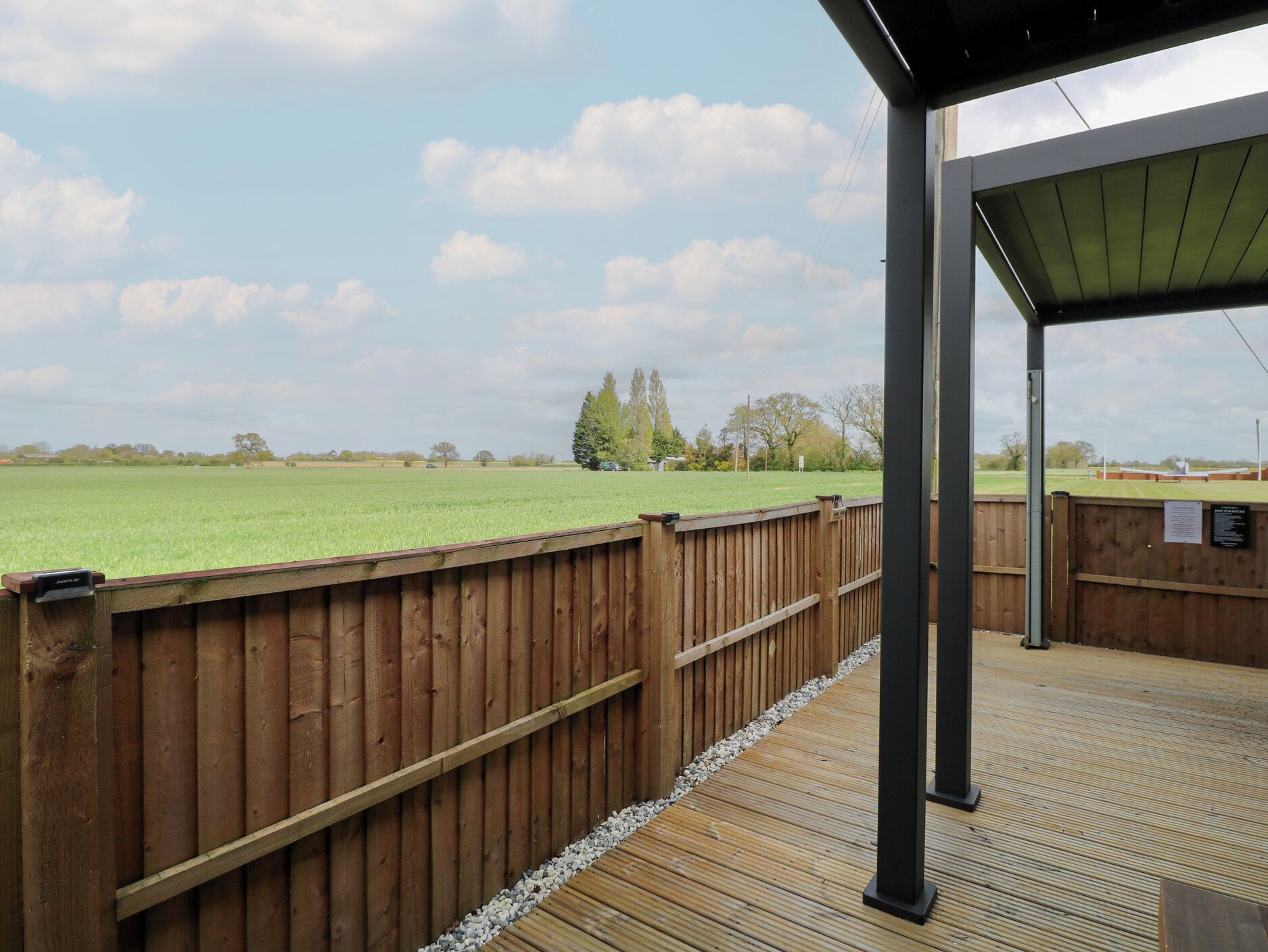 A wooden deck with a view of a green field and trees in the distance.