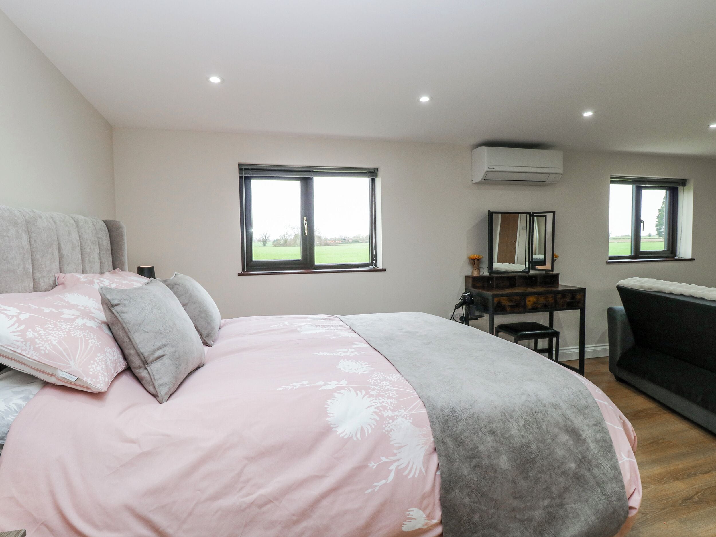 Un dormitorio con cama, escritorio, silla y sofá. Hay dos ventanas y un equipo de aire acondicionado.