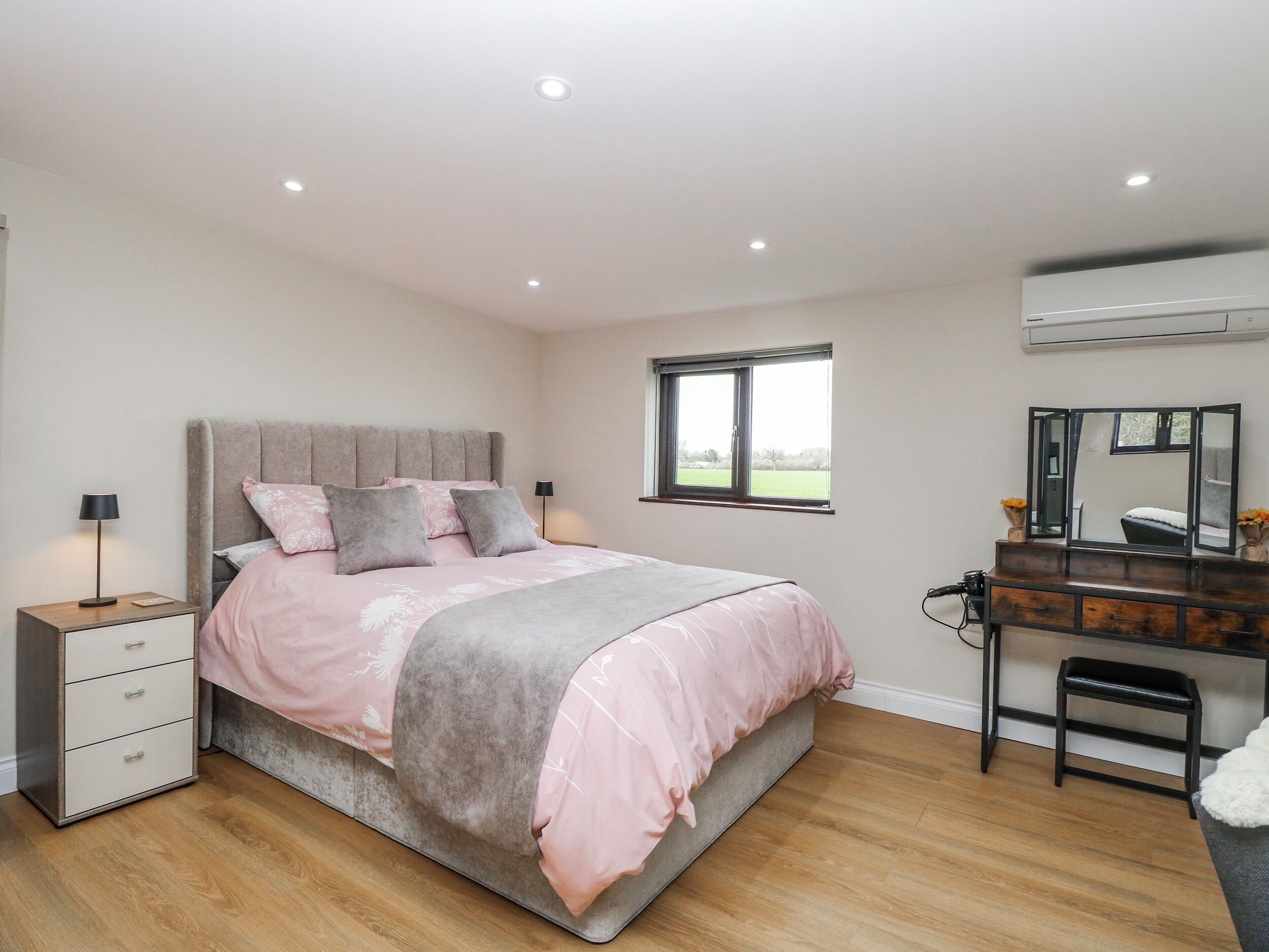 A bedroom with a bed, bedside tables, a dresser, a mirror, and a window.