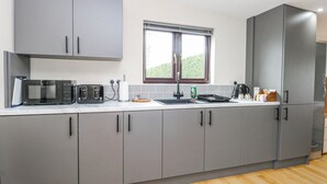 Cozinha moderna com armários cinza, micro-ondas, torradeira e janela com vista para o verde.