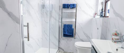 A modern bathroom with a glass-enclosed shower, a white toilet, and a sink with a mirror.