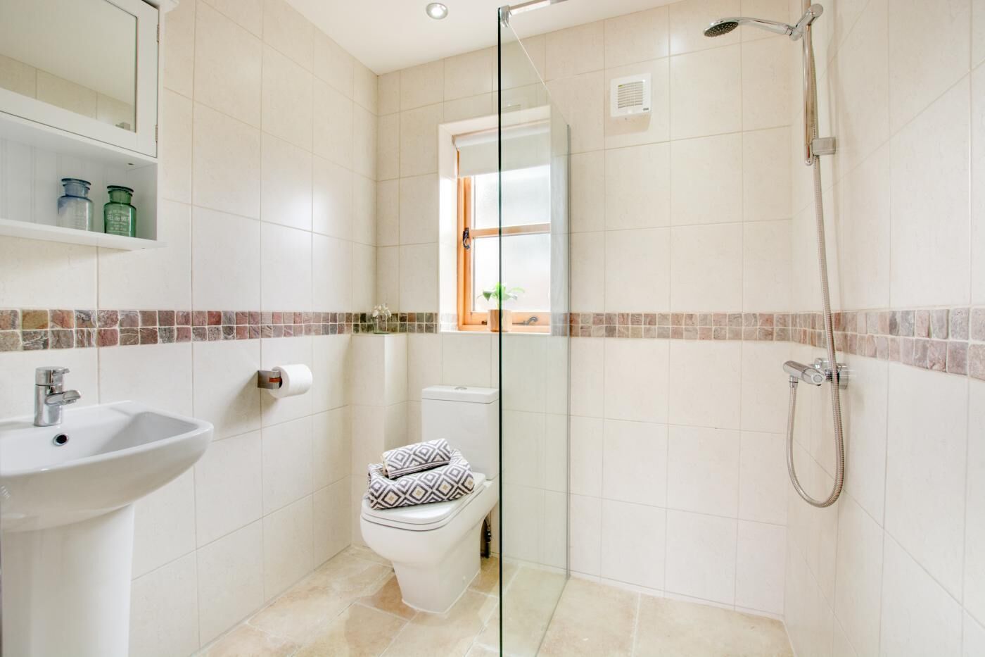 A bathroom with a glass-enclosed shower, a sink, a toilet, and a window.