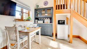 Una cocina con una mesa de comedor, sillas, un refrigerador y una escalera de madera.