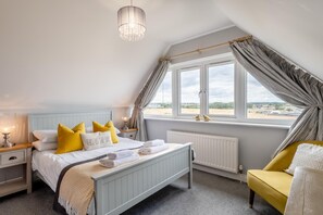 Une chambre à coucher avec un lit, des tables de chevet, une fenêtre avec des rideaux, un radiateur et une vue sur l’extérieur.