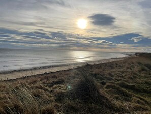 Eine Küstenlandschaft mit Strand, grasbewachsenen Dünen und blauem Himmel.
