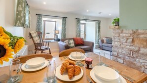A dining area with a table set for breakfast, including croissants and jam, and a view of a living room with a sofa and a stone fireplace. - 2 Bed in Nenthead (oc-s32235) (Alston Moor)