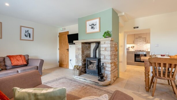 A living room with a stone fireplace, a sofa, a dining table, and a kitchen in the background. - 2 Bed in Nenthead (oc-s32235) (Alston Moor)
