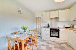 Une cuisine compacte avec des meubles blancs, un four encastré et un coin repas comprenant une table et des chaises en bois.